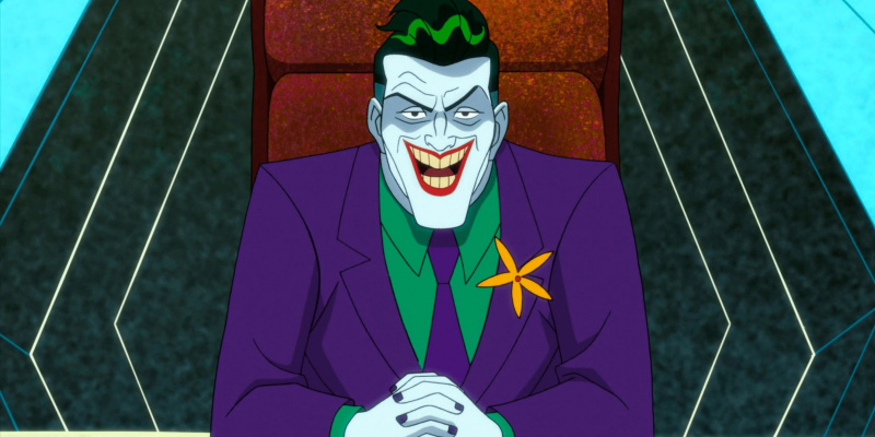   हार्ले क्विन का जोकर अपनी लाल कुर्सी पर बैठे हुए एक खतरनाक मुस्कान के साथ मुस्कुराता है।